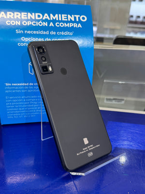 A black smartphone shown from the back, leaning on a clear display stand on a blue surface, with a blue promotional sign behind it.