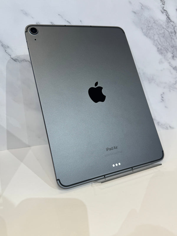 A dark gray Apple iPad Air tablet standing upright on a white surface against a light marble-patterned background.