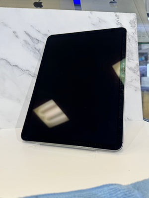 A black Apple iPad tablet displayed on a clear stand against a white marble-patterned backdrop.