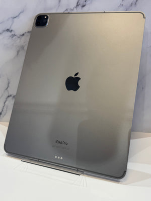 A silver Apple iPad Pro standing upright on a clear acrylic stand against a white marble background. 