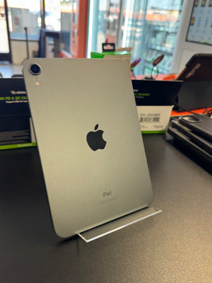 A silver Apple iPad standing upright on a small clear display stand on a dark tabletop, with the Apple logo visible on the back.