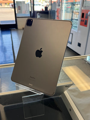 A gold Apple iPad Pro tablet standing upright on a clear display stand inside a retail store, showing the back of the device with the Apple logo and 'iPad Pro' text.