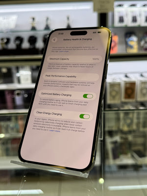 A smartphone displaying the Battery Health & Charging settings screen, photographed in a retail or showroom environment with blurred display cases in the background.