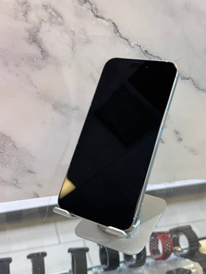 A silver smartphone with a black screen stands on a small metallic display stand against a white marble-patterned background.