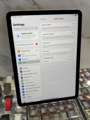 An iPad displaying the Settings app, photographed in a retail or showroom environment with a marble-like wall and display cases in the background.