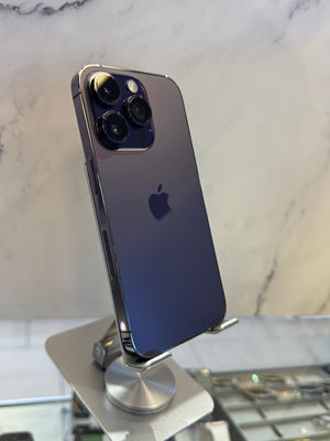 A dark blue-purple Apple iPhone 12 Pro Max with a triple-camera system, displayed on a silver metal stand against a light marble-patterned background.