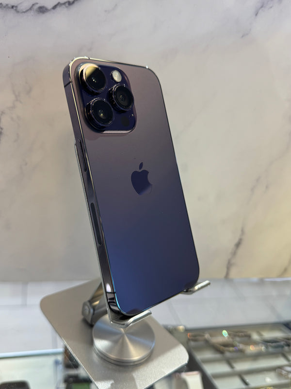 A dark blue-purple Apple iPhone 12 Pro Max with a triple-camera system, displayed on a silver metal stand against a light marble-patterned background.