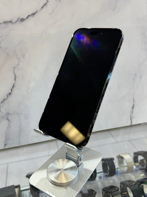 A black smartphone displayed upright on a metallic stand, with a marble-patterned wall behind it and watch displays visible in the foreground.