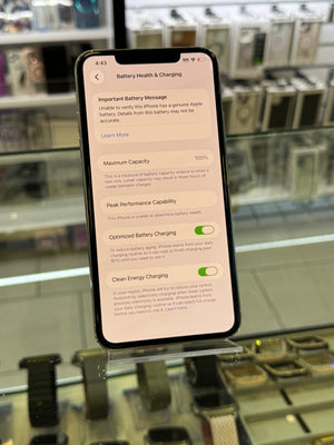 A black smartphone displayed vertically on a glass stand inside a retail store. The phone screen is on and shows a settings page with battery-related options and text.