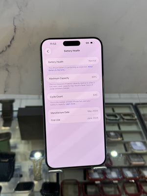 A black smartphone displaying the Battery Health settings screen on its screen, resting on a display stand in front of a watch and case display case.