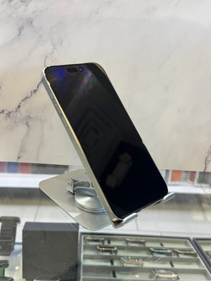 A silver smartphone with a black screen is displayed on a metallic stand inside what appears to be a jewelry or watch display case, with a marble-patterned background.
