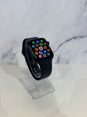 A black smartwatch with a black band and a colorful digital watch face, displayed on a clear stand against a white marble-patterned background.
