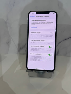 A black smartphone displayed upright on a small stand, showing the Battery Health & Charging settings screen on a light marble-patterned background.