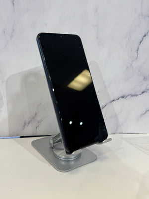 A black smartphone displayed at an angle on a silver metal stand, set against a white marble-patterned background.