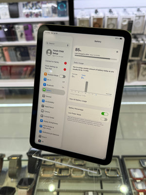 A tablet device with a black bezel and a white user interface screen, photographed in a retail or display environment with glass cases in the background.