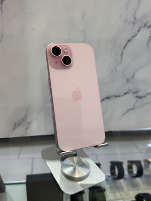 A pink Apple iPhone 12 Pro shown from the back, resting on a silver metal display stand against a white marble-patterned wall.