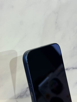 Close-up of the top-left corner of a dark blue smartphone with a black screen, resting on a white marble surface.