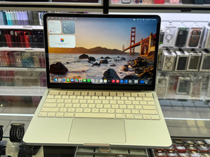 A silver aluminum laptop with a matching keyboard and trackpad, shown open on a retail display counter with a San Francisco Golden Gate Bridge desktop wallpaper. The background shows shelves of other electronic accessories.
