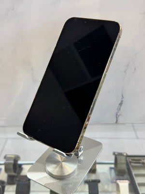 A black smartphone with a gold-toned edge, displayed upright on a silver metal stand against a light marble-patterned background.