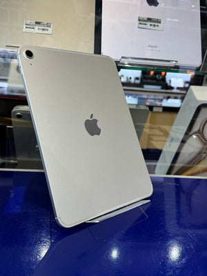 A silver Apple iPad Pro shown from the back, standing on a small display stand on a glossy blue counter inside a retail store.