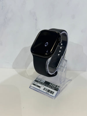 Black smartwatch with a square rounded-rectangle face and black band, displayed on a clear acrylic stand against a light gray marble-patterned background.