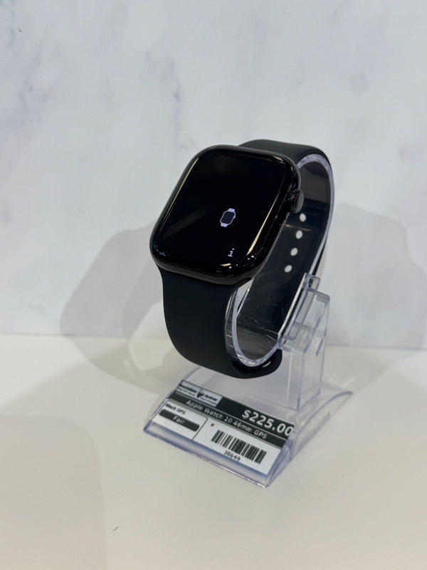 Black smartwatch with a square rounded-rectangle face and black band, displayed on a clear acrylic stand against a light gray marble-patterned background.