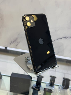 A black Apple iPhone with a glossy finish, standing on a silver metal display stand. The back of the phone is visible, showing the dual camera lenses and the Apple logo.