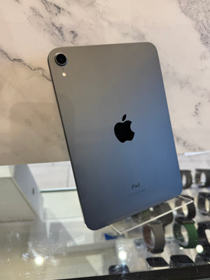 A gray Apple iPad shown from the back, resting on a clear display stand on a glass counter with a marble-patterned background.