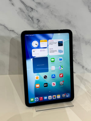 A black iPad Pro tablet standing upright on a clear acrylic display stand against a white marble-patterned background.