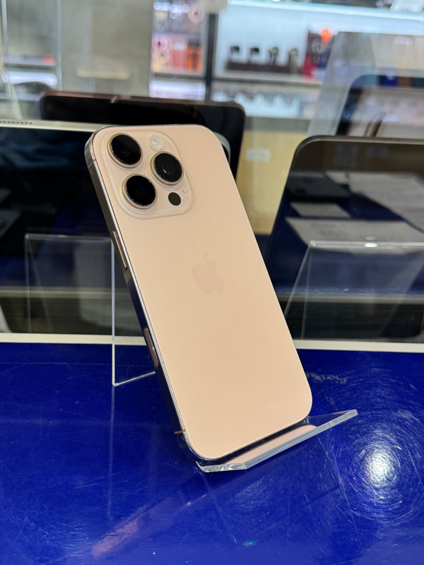 A gold-colored Apple iPhone 12 Pro shown from the back, resting on a clear plastic display stand on a blue counter inside a store.