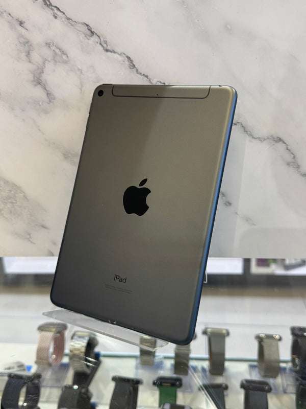 An Apple iPad tablet shown from the back, featuring a metallic gray finish and a black Apple logo, displayed on a clear stand in front of a white marble-patterned background.