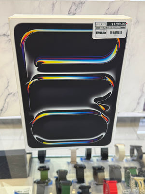 A boxed Apple product, likely an iPad, shown in its original retail packaging with a black front panel featuring the signature glossy rainbow-colored abstract design and a price sticker in the top right corner.