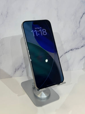 A silver metal phone stand holding a smartphone with a dark blue and green lock screen, set against a white marble-patterned background.