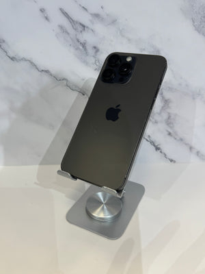 A dark gray Apple iPhone Pro shown from the back, resting on a silver metal stand against a white marble-patterned background.