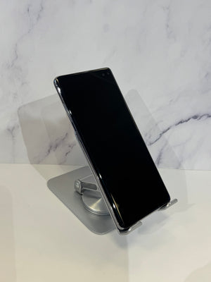 A black smartphone with a glossy screen, displayed at an angle on a silver metal stand against a white marble-patterned background.