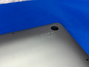 Close-up of the back corner of a dark gray laptop or tablet showing handwritten markings, placed on a bright blue textured surface.