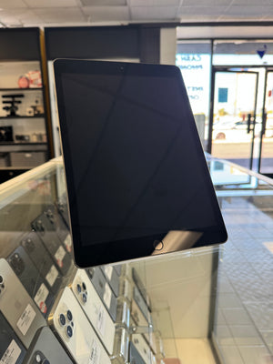 A black tablet with a glossy screen, standing on a glass display counter inside a retail store.