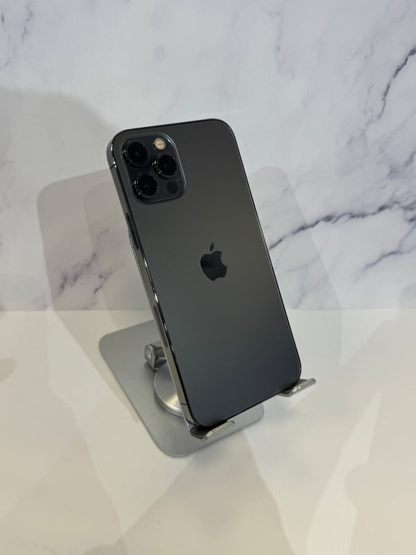 A dark gray Apple iPhone 12 Pro shown from the back, resting on a silver metal stand against a white marble-patterned background.