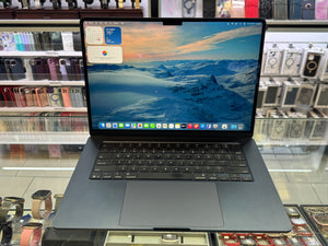 Laptop on a glass table with a mountainous landscape on the screen, surrounded by electronic items.