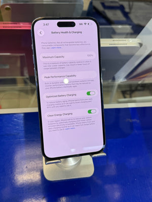 A black smartphone displayed upright on a stand, showing the Settings screen for Battery Health & Charging on a blue surface with a blurred indoor background.