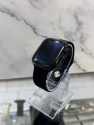 A black smartwatch with a square screen and black band, displayed on a clear acrylic stand against a white marble-patterned background.