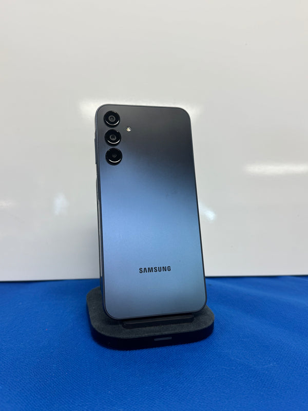 A Samsung smartphone shown from the back, standing upright on a small black display stand against a white backdrop with a blue surface below.