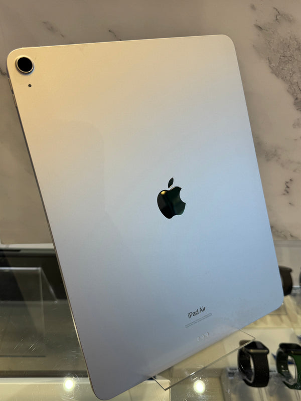 Silver Apple iPad Air shown from the back, standing on a glass display stand in a store setting with a marble-patterned wall behind it.