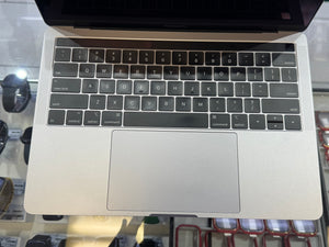 Close up on an Apple Macbook black keyboard displayed on a glass shelf with smartwatches and accessories in the background. 