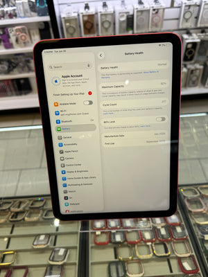 A tablet device with a dark red or black bezel and a light gray screen showing settings menus, photographed in a retail display case with shelves of watch cases visible in the background.