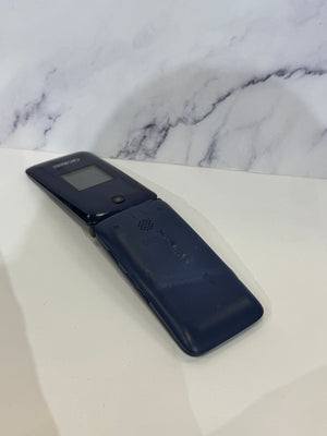 A dark navy blue flip phone, identified as a Samsung, resting on a white surface with a white and gray marble-patterned background.