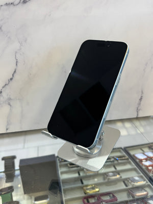 A black smartphone with a silver edge, resting on a metallic stand in front of a marble-patterned wall and watch display case.