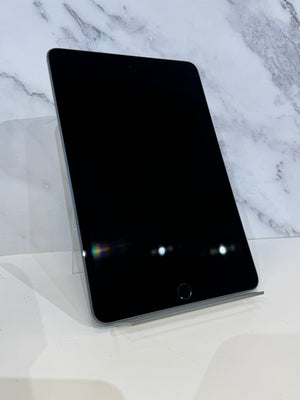 A black tablet device with rounded corners and a home button, displayed upright on a clear stand against a white marble-patterned background.