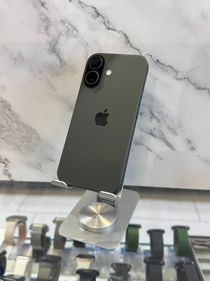 A dark gray Apple iPhone shown from the back, resting on a silver metal display stand in front of a white marble-patterned wall.