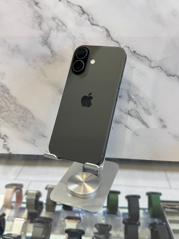 A dark gray Apple iPhone shown from the back, resting on a silver metal display stand in front of a white marble-patterned wall.
